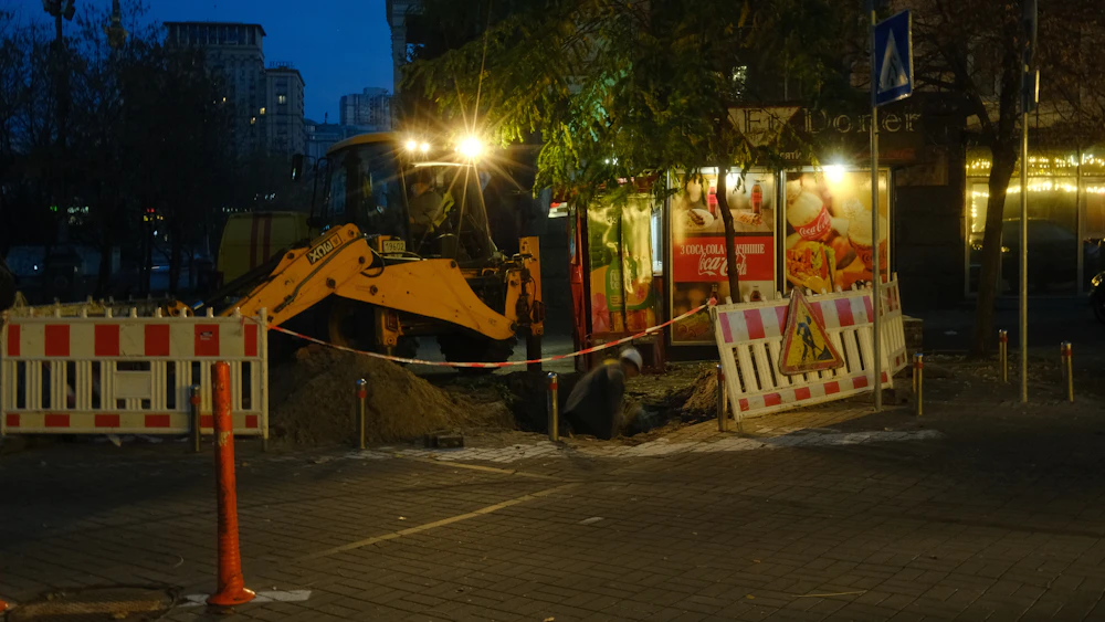 An excavator and safety barriers at a street excavation after dark